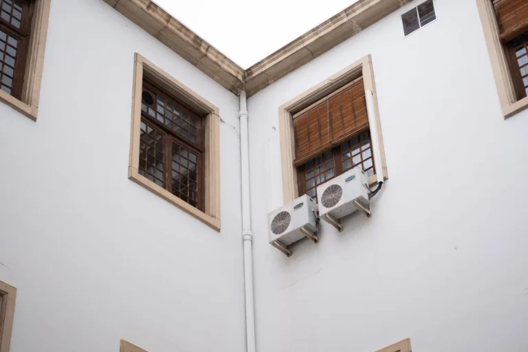 Dos unidades exteriores de aire acondicionado instaladas bajo una ventana de una fachada blanca tradicional