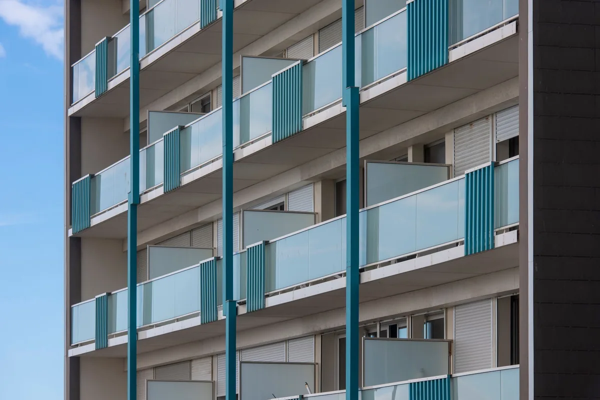 Fachada de un edificio de apartamentos de varias plantas con balcones de cristal y barandillas azules