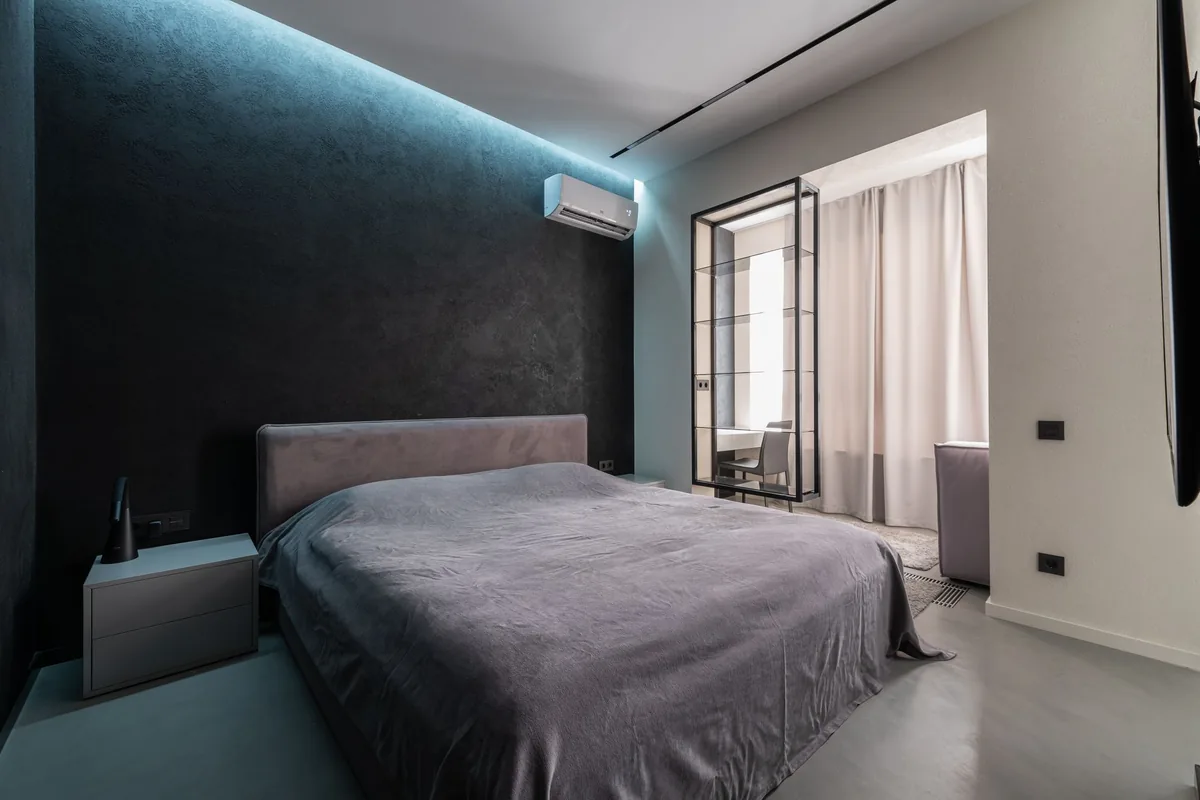 Dormitorio con un split de pared sobre la cabecera de la cama y una luz azulada en el techo