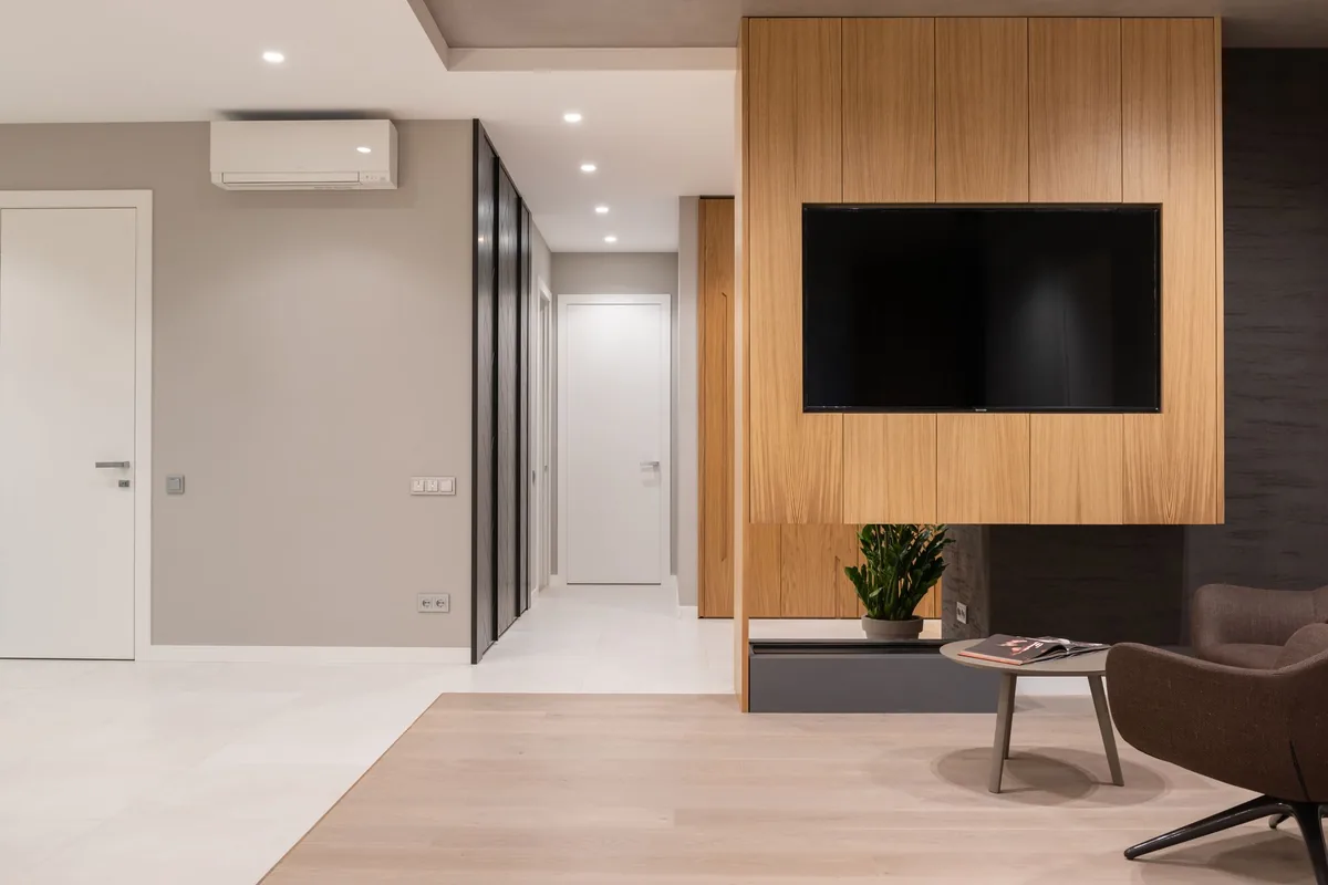 Salón moderno con un split de pared blanco sobre un pasillo y un televisor en un mueble de madera