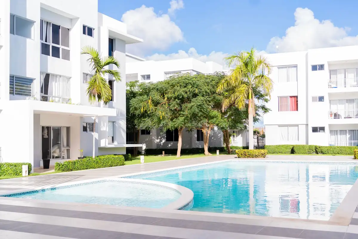 Complejo de apartamentos blancos de tres plantas con palmeras y una piscina al sol