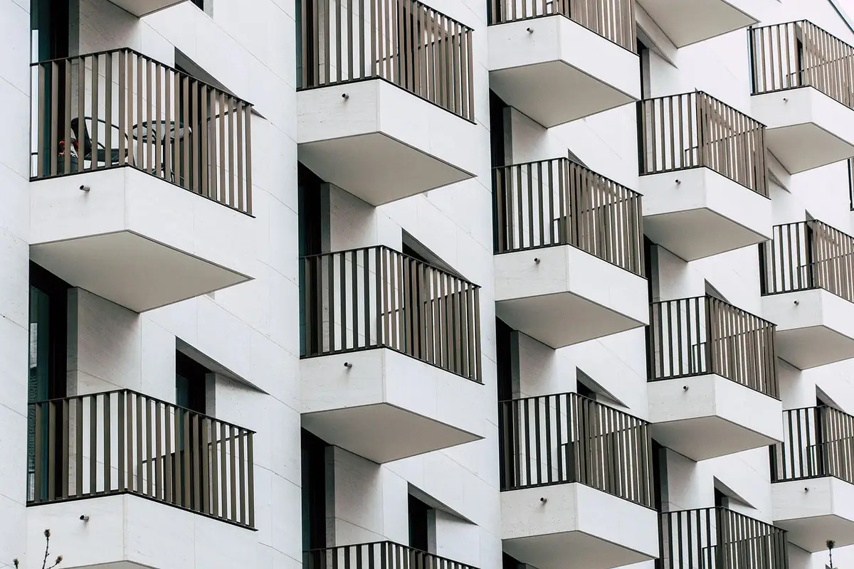 Fachada blanca de un bloque de pisos con balcones de barandilla de listones