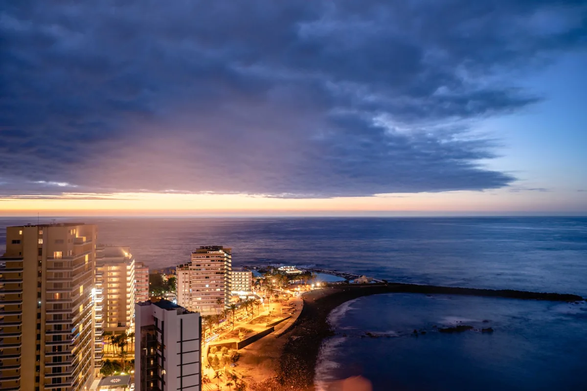 Torres de pisos junto al mar al anochecer, con un paseo iluminado y un espigón
