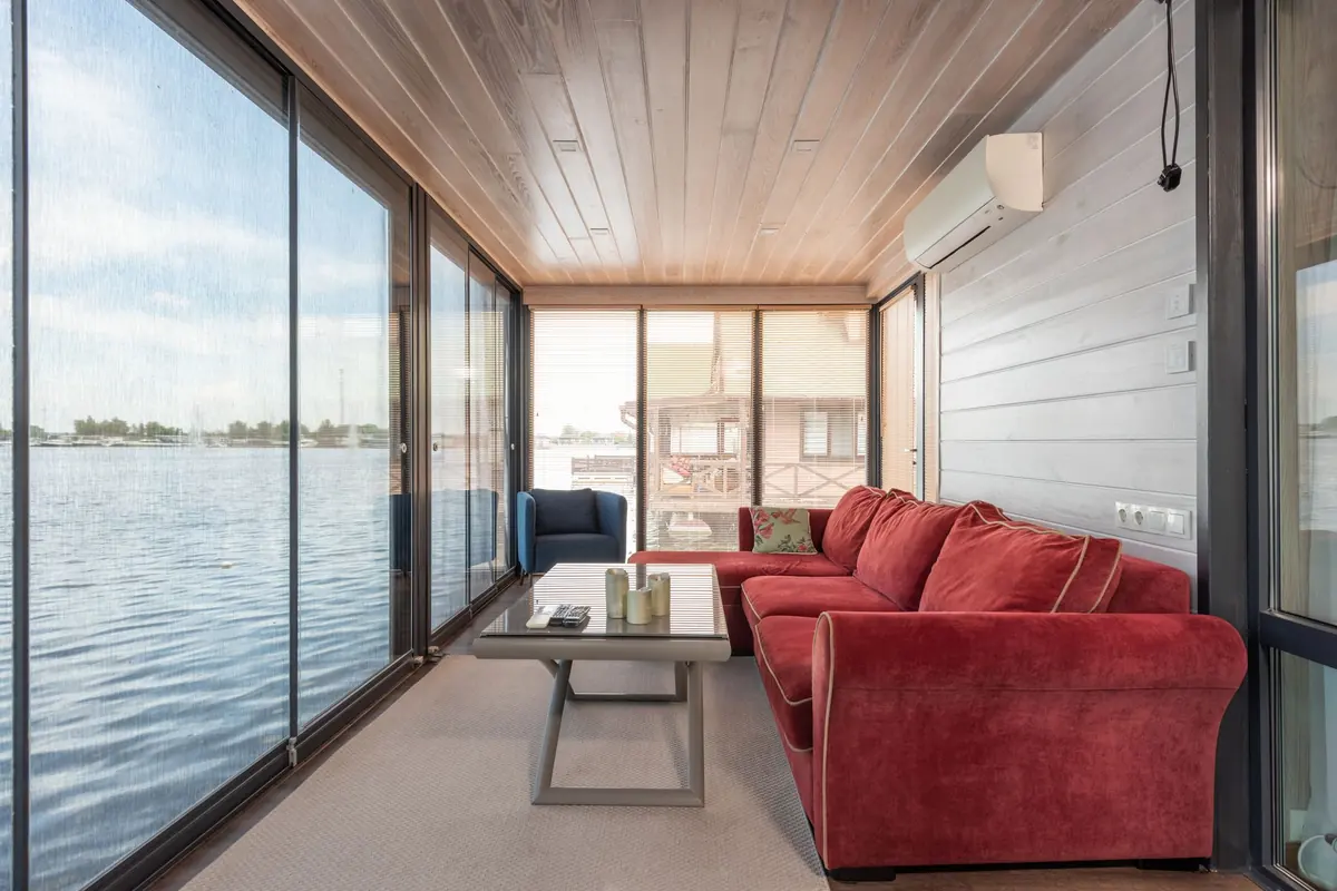 Salón con sofá rojo y ventanales sobre el agua, con un split blanco en la pared lateral