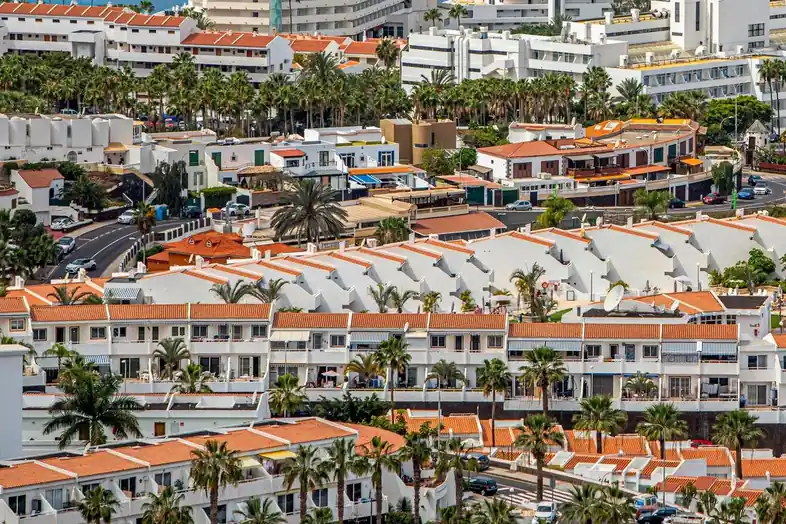 Conjuntos de apartamentos blancos de pocas plantas, con terrazas y palmeras, vistos desde el aire en Tenerife