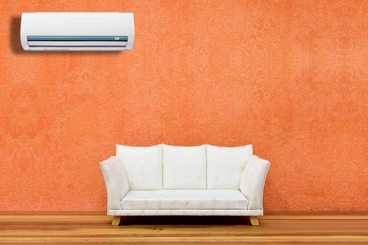 Split de aire acondicionado blanco colgado de una pared naranja, sobre un sofá blanco