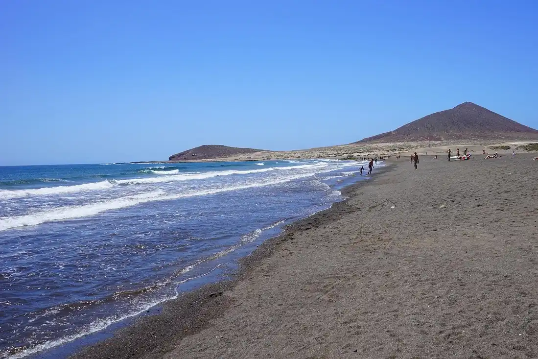 Playa de El Médano, en Tenerife, con olas y una montaña al fondo