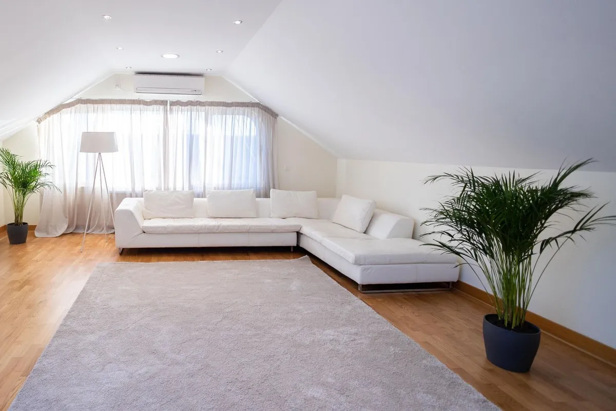 Split de aire acondicionado blanco en la pared de un salón luminoso con sofá blanco y cortinas