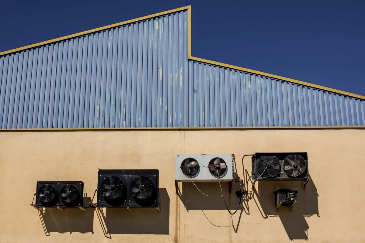 Unidades exteriores con ventilador colgadas de la pared de una nave de chapa azul