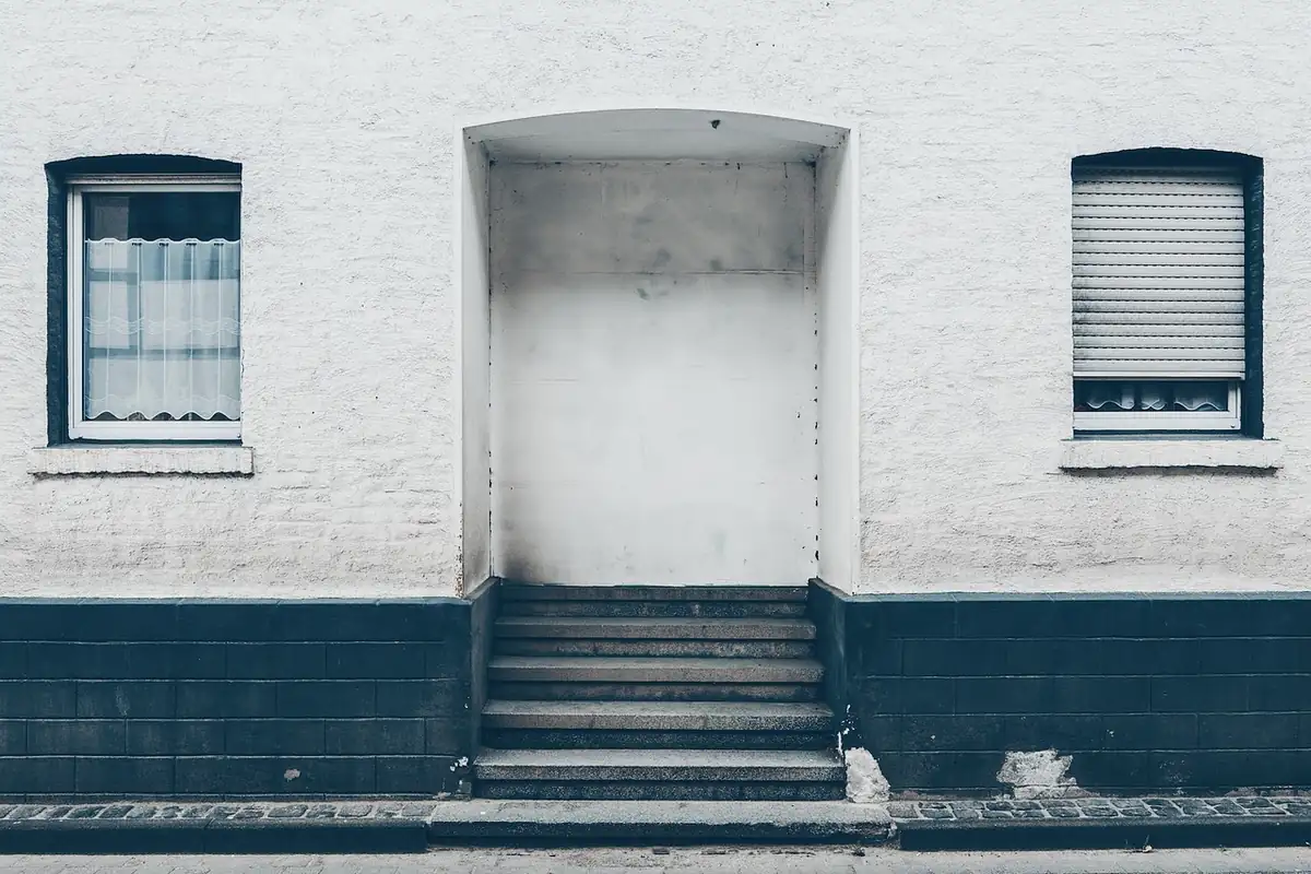Fachada blanca con dos ventanas, una con persiana, y un portal con escalones