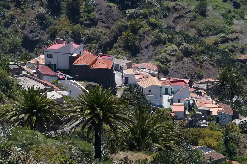 Pueblo de montaña con casas blancas de tejado rojo entre palmeras en una ladera verde