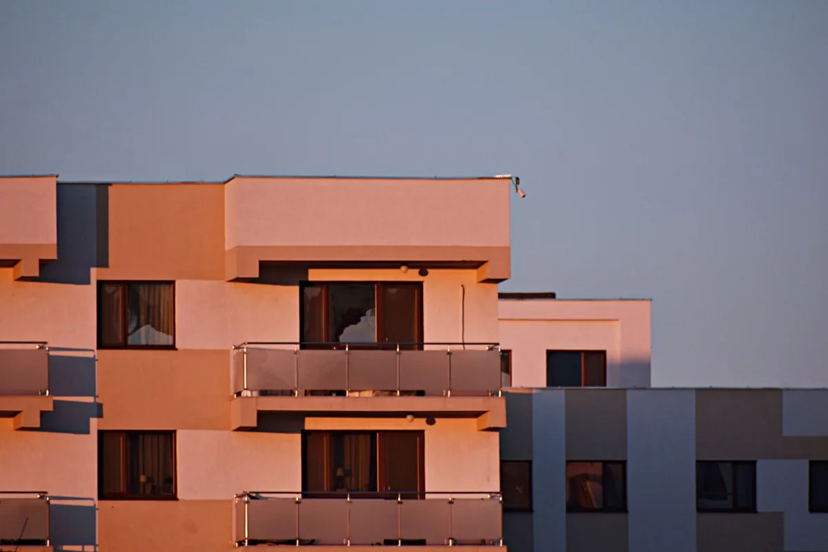 Fachada de un edificio de apartamentos con balcones de cristal y la luz anaranjada de la tarde sobre la pared