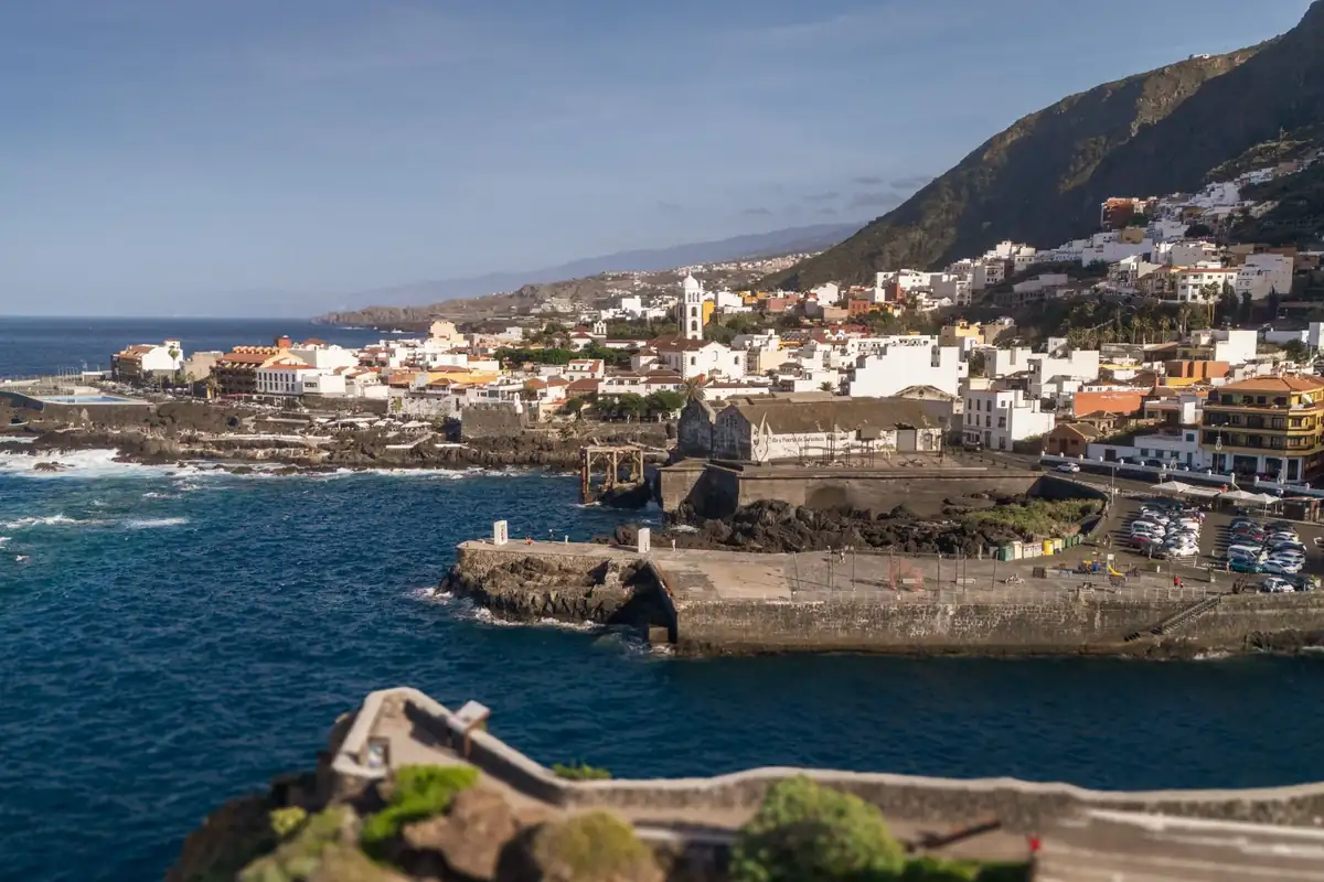 El casco de Garachico visto desde el mar, con casas blancas, un campanario y la ladera detrás