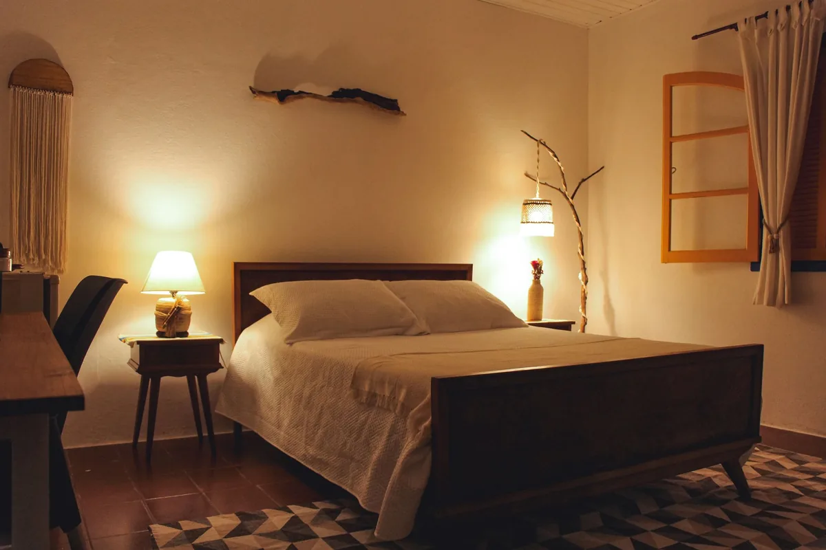 Dormitorio de noche con dos lámparas encendidas junto a una cama de madera