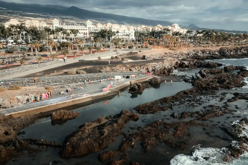Costa de Alcalá con piscinas naturales entre rocas, un hotel entre palmeras y las montañas al fondo