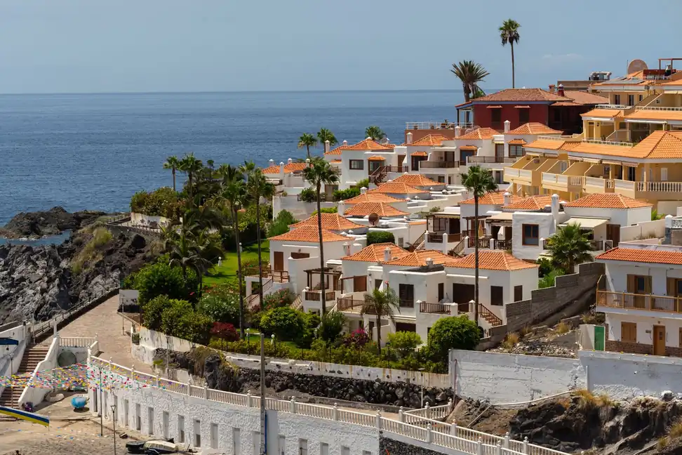 Viviendas bajas de tejas naranjas escalonadas sobre una cala de la costa de Tenerife, con el mar al fondo