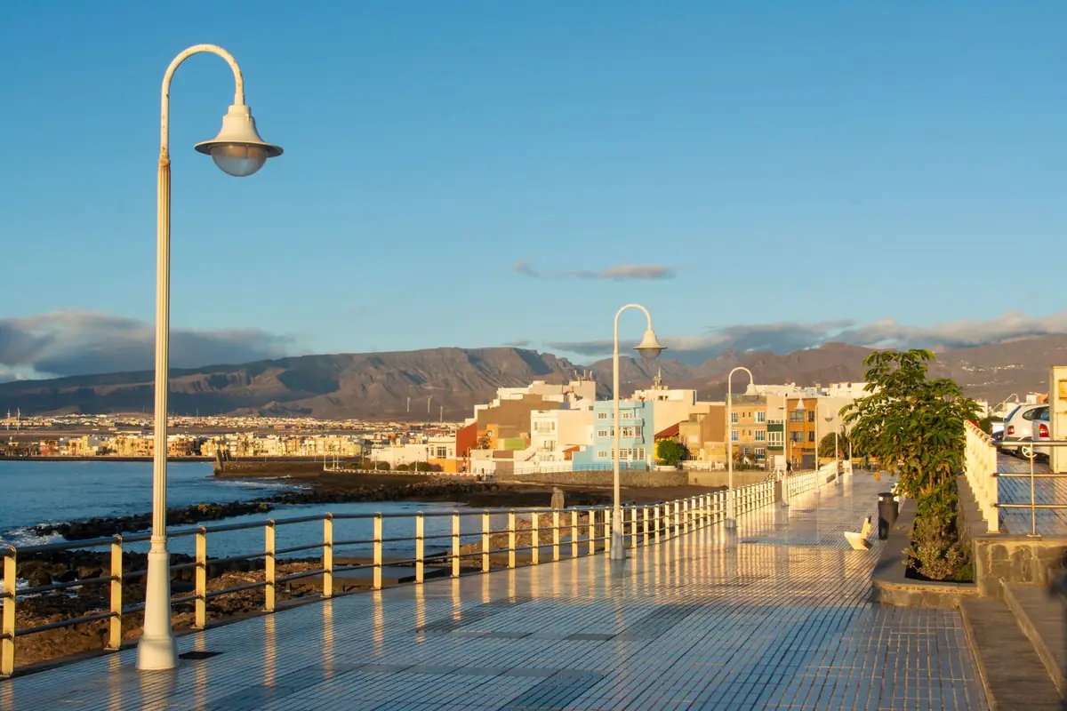 Paseo marítimo con farolas junto al mar y edificios de colores de pocas plantas en una costa de Canarias