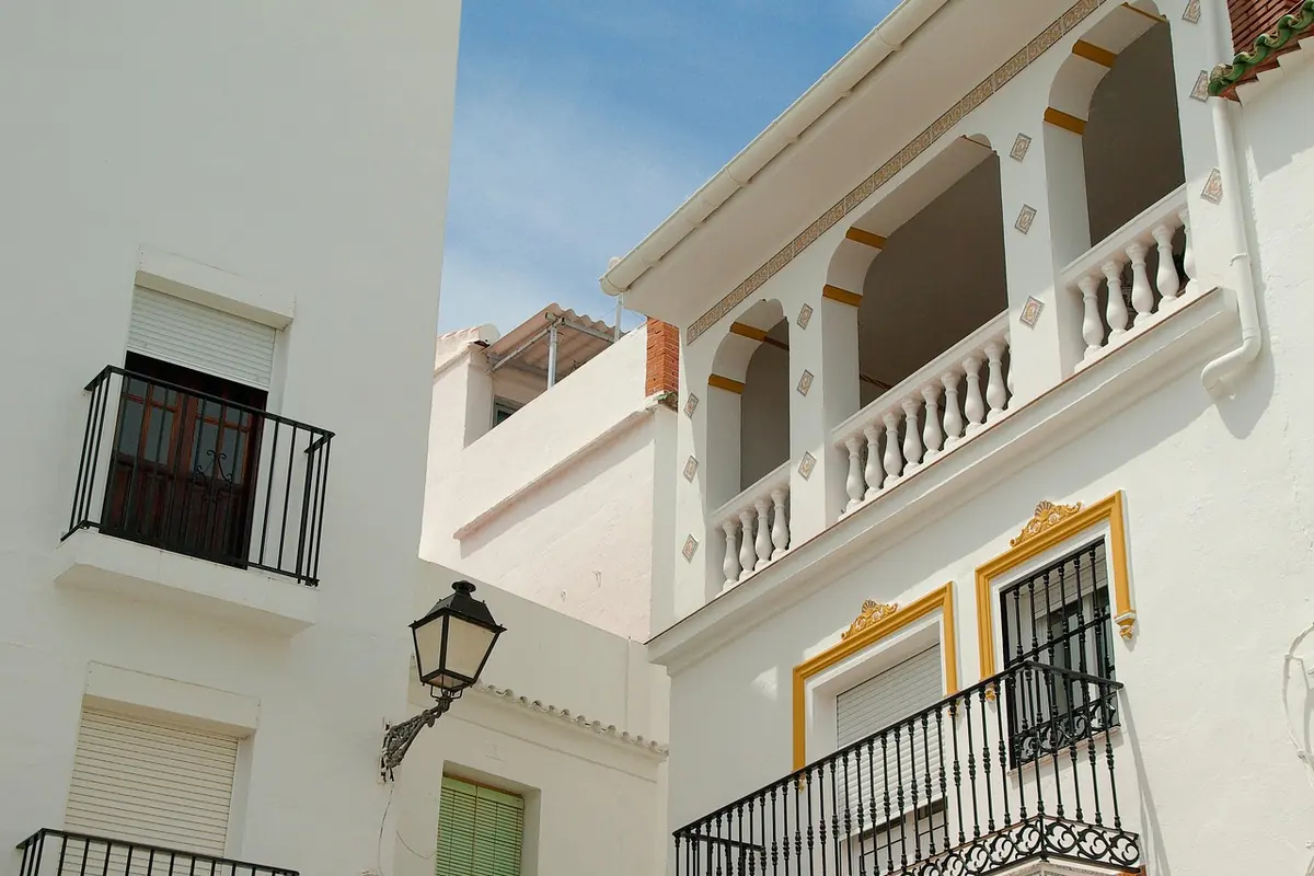 Fachada blanca de un edificio de viviendas con balcones, persianas y un farol