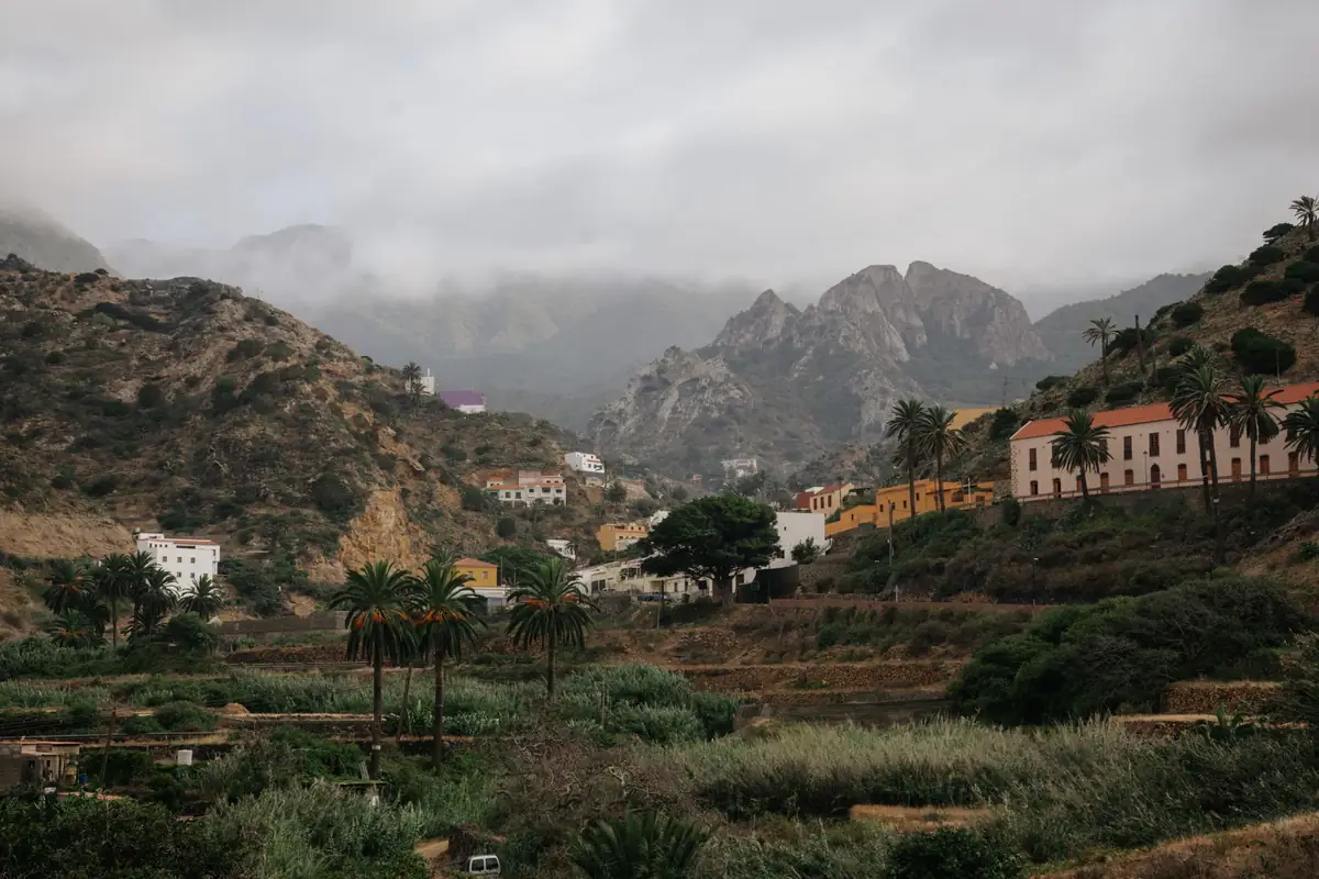 Pueblo de casas de colores entre palmeras en un valle de montaña de Canarias, con nubes bajas
