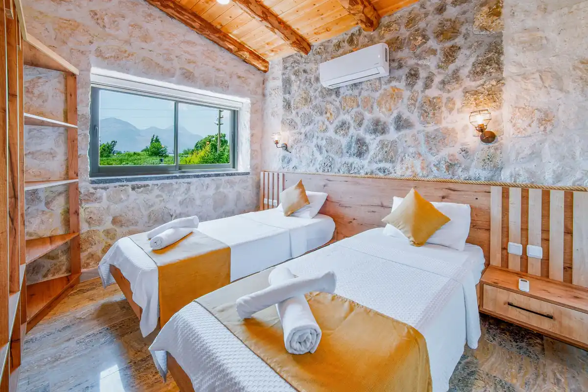 Dormitorio con muros de piedra, techo de madera y un split de pared sobre las camas