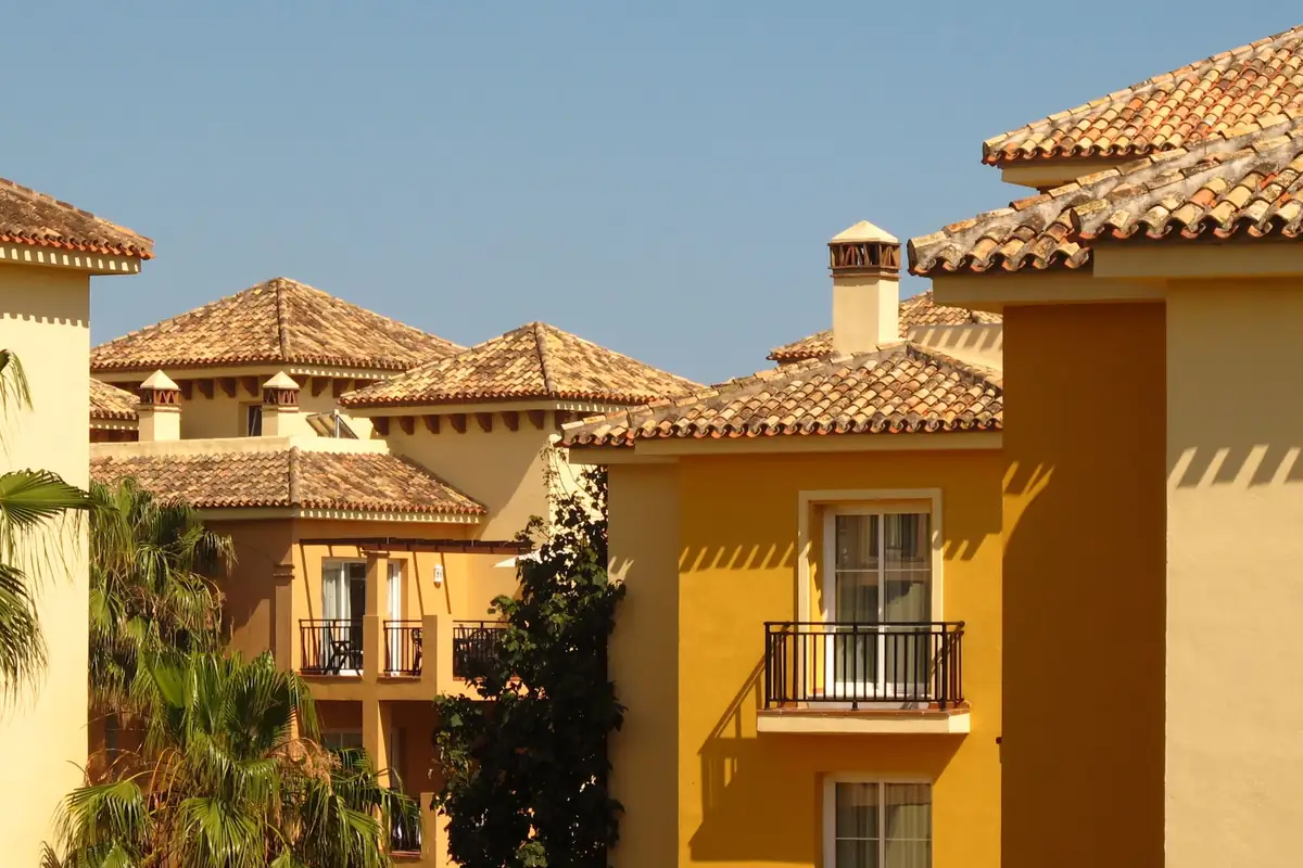Casas de fachada amarilla con tejados de teja y balcones de hierro bajo un cielo despejado