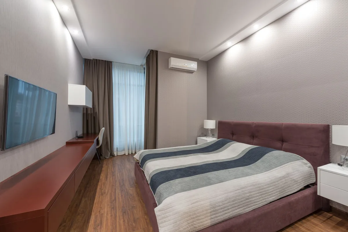 Dormitorio con una cama de colcha a rayas, un televisor en la pared y un split en la pared del fondo
