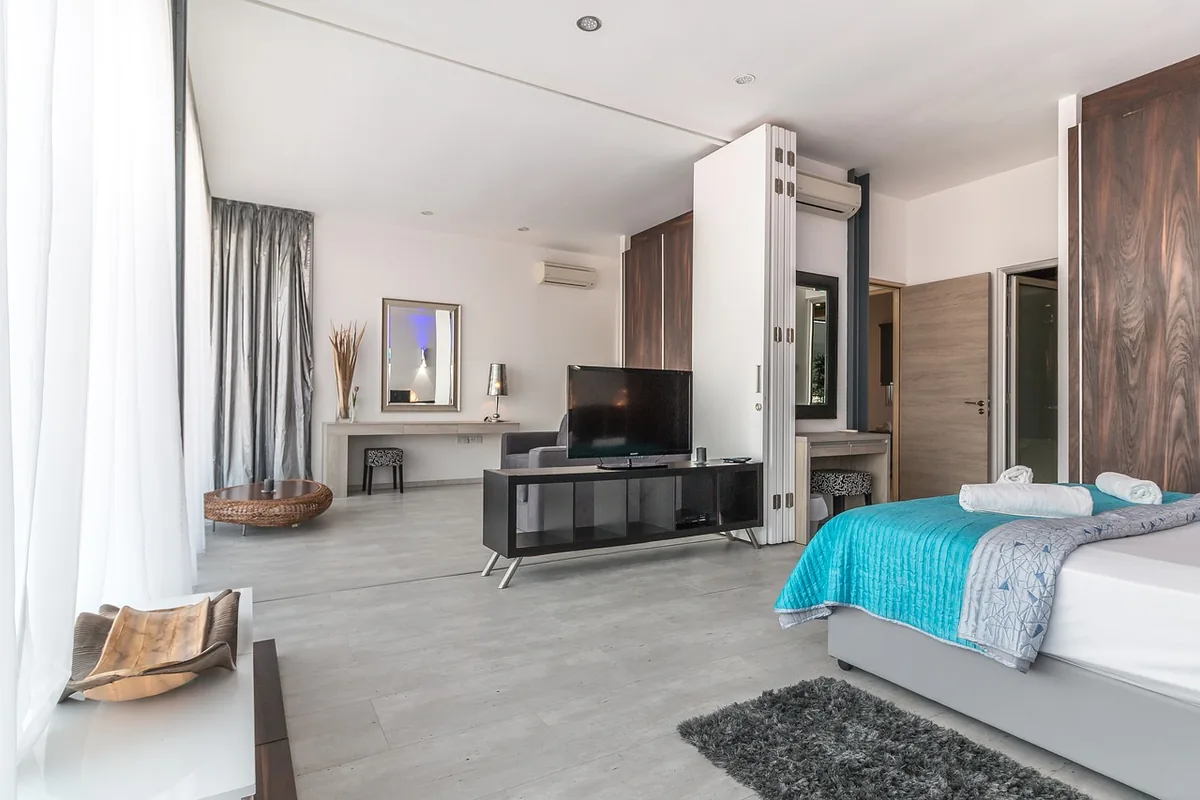 Habitación de hotel amplia con una cama de colcha turquesa, un televisor y dos splits de pared
