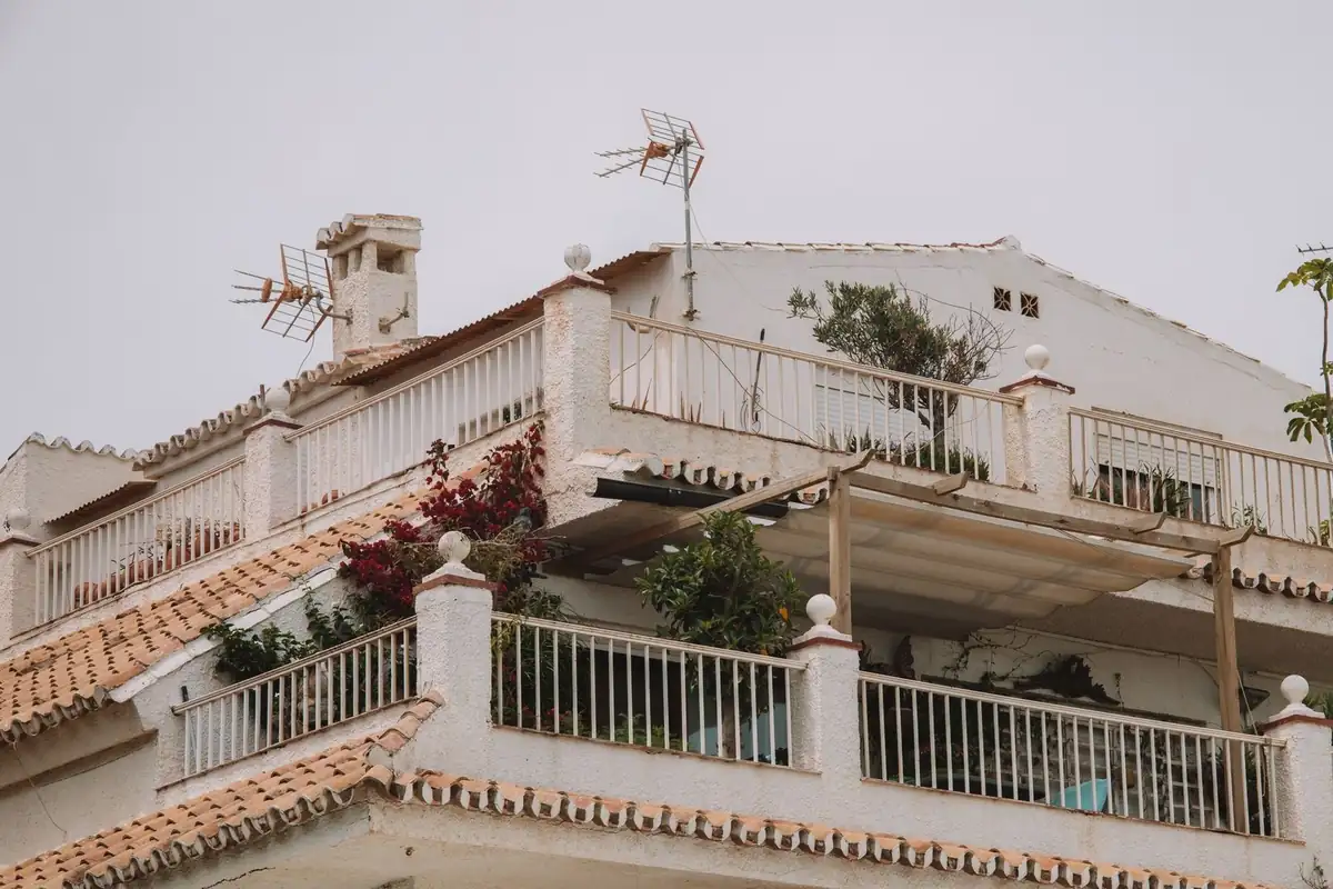 Edificio blanco con terrazas, tejado de teja y antenas en la azotea