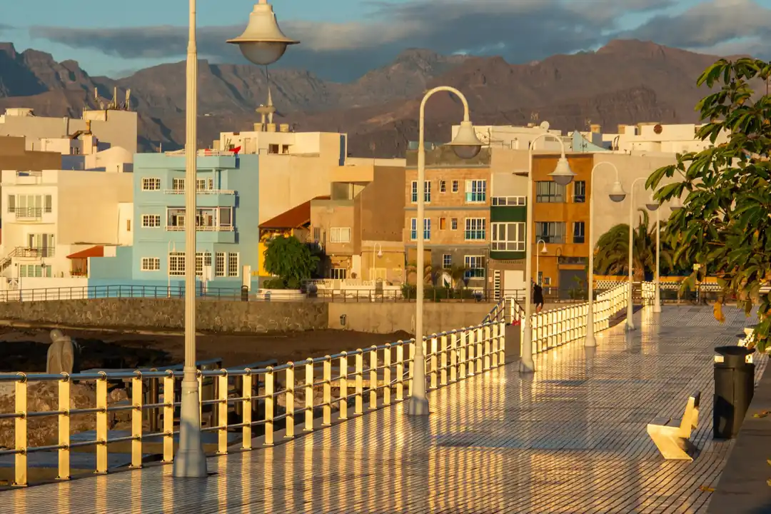 Paseo marítimo al atardecer con edificios de varias plantas y montañas al fondo