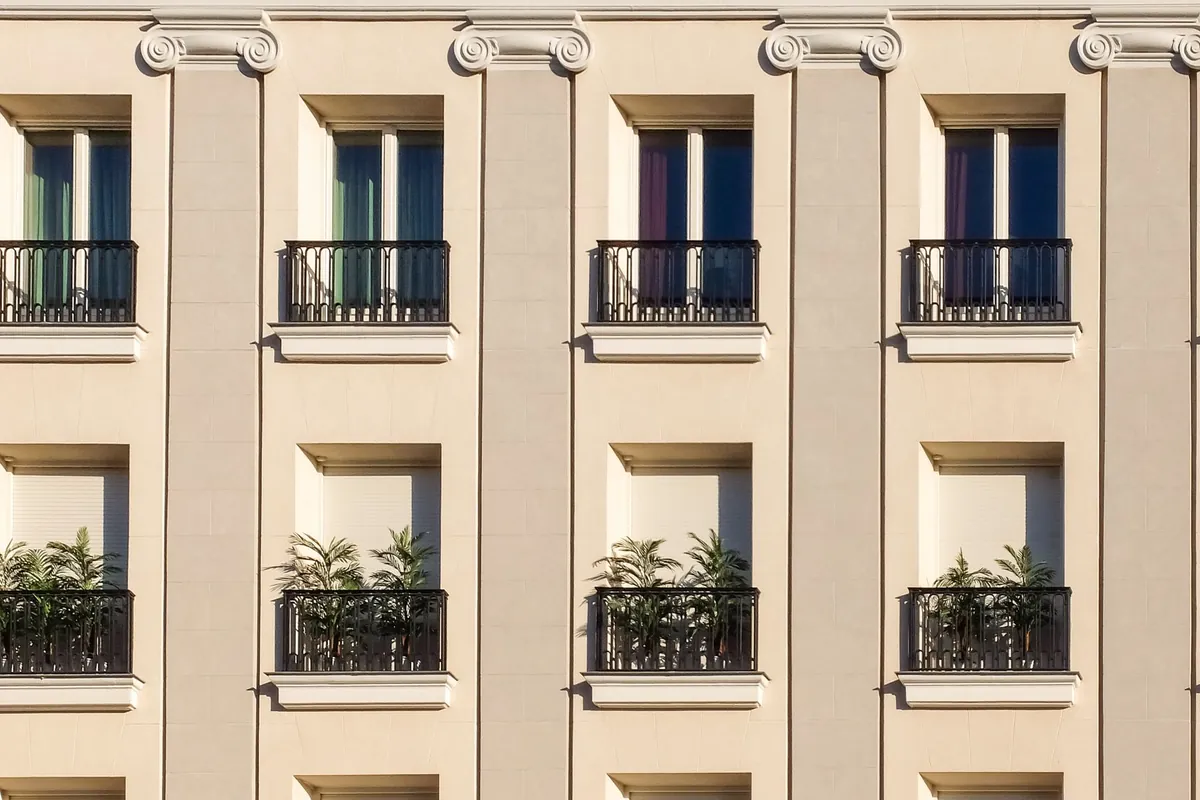 Fachada clara de un edificio de pisos con balcones de forja y plantas en las barandillas