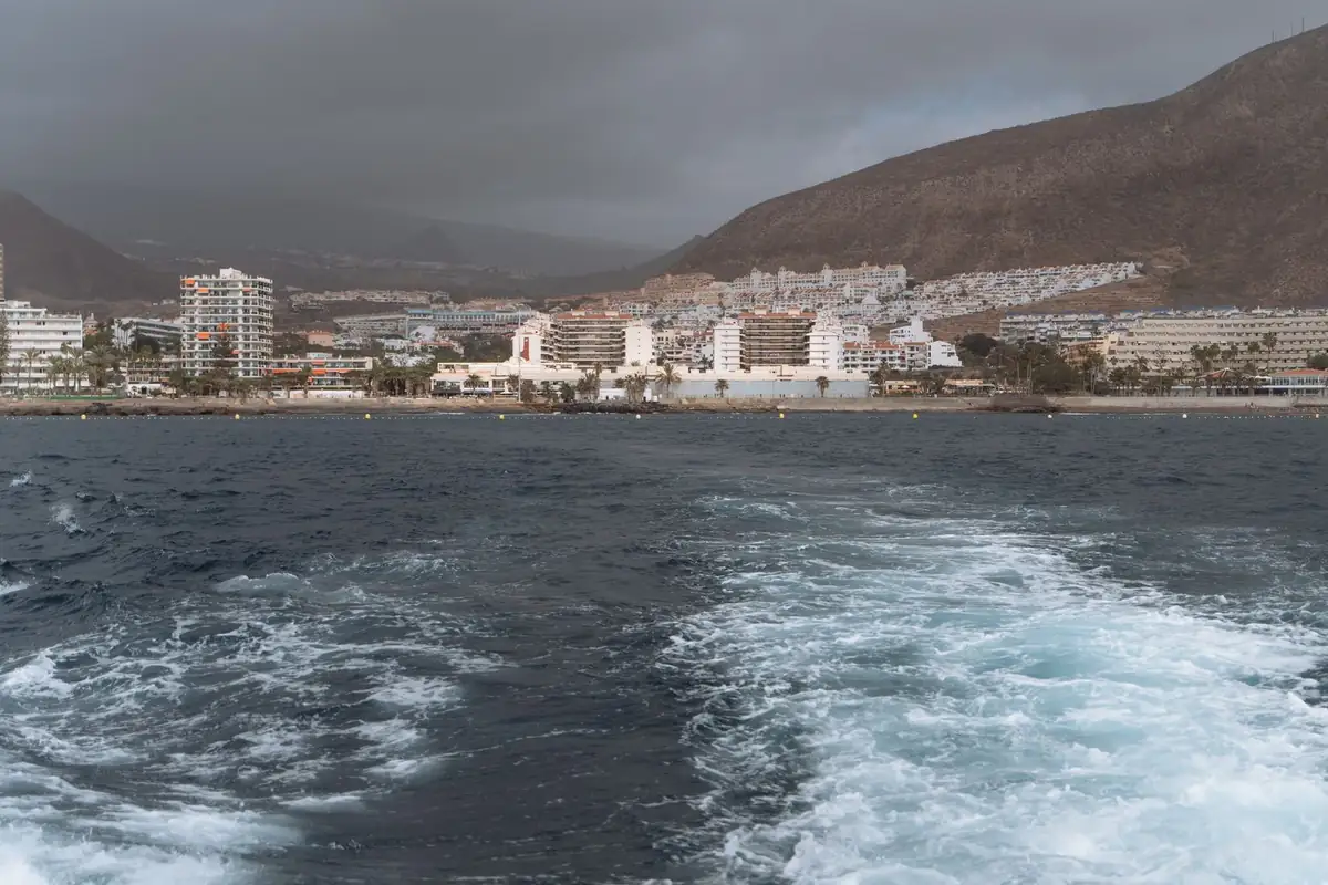 Costa de Los Cristianos vista desde el mar, con bloques de apartamentos al borde del agua y una montaña detrás