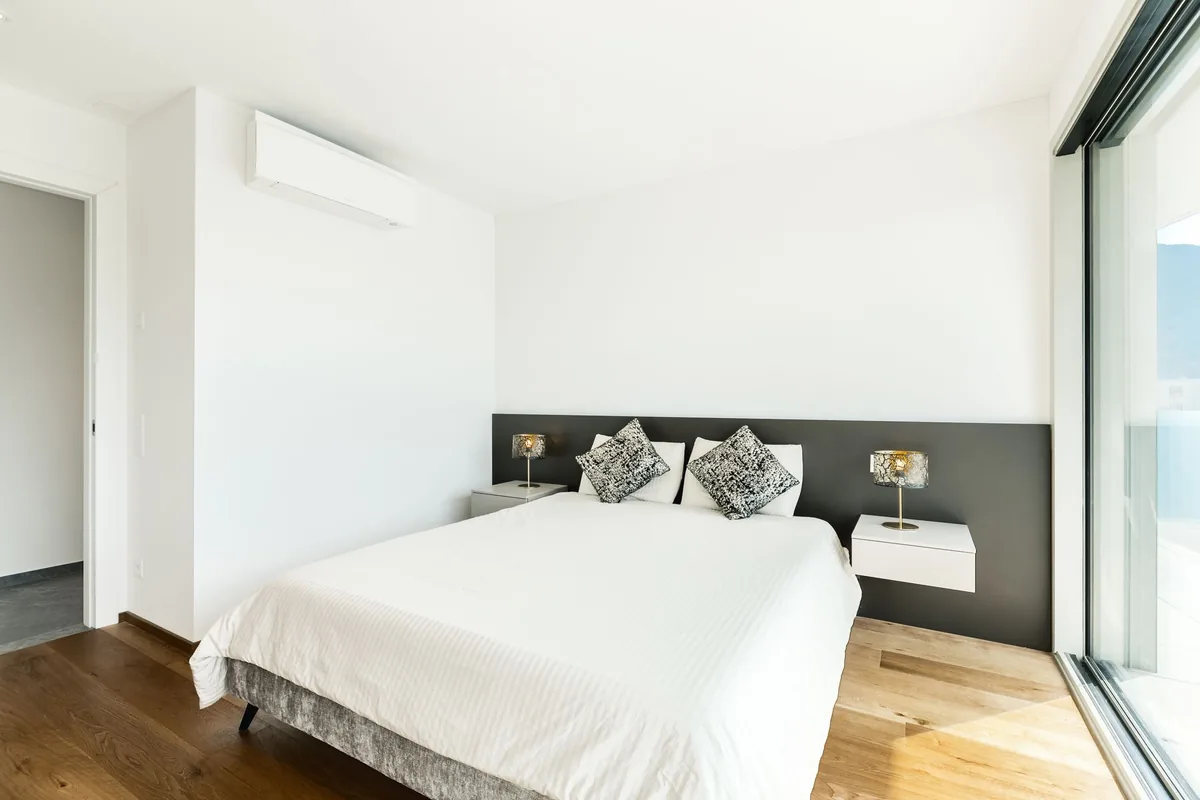 Dormitorio blanco y luminoso con un split de pared, una cama doble y una ventana corredera
