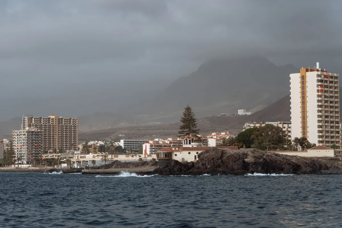 Olas contra las rocas de la costa de Los Cristianos, con torres de apartamentos pegadas al mar