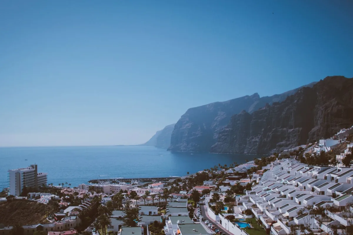 Edificios blancos escalonados entre palmeras, al pie de unos acantilados y junto al mar