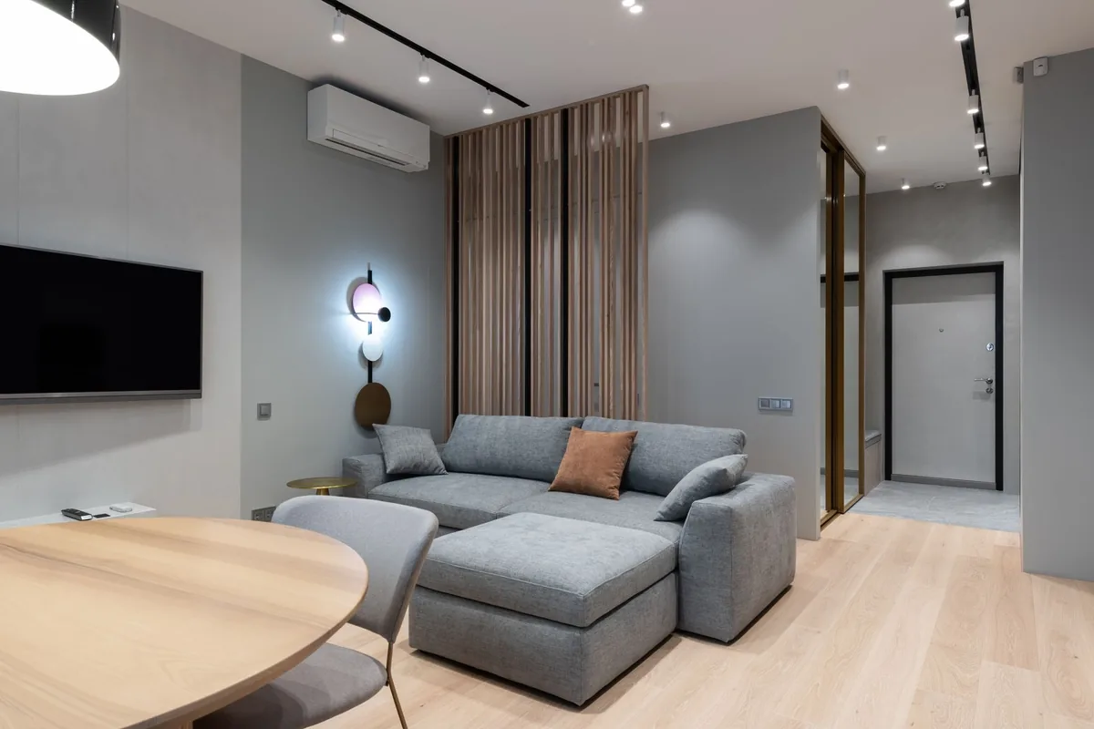 Salón de un apartamento con un sofá gris en esquina y un split de pared blanco cerca del techo