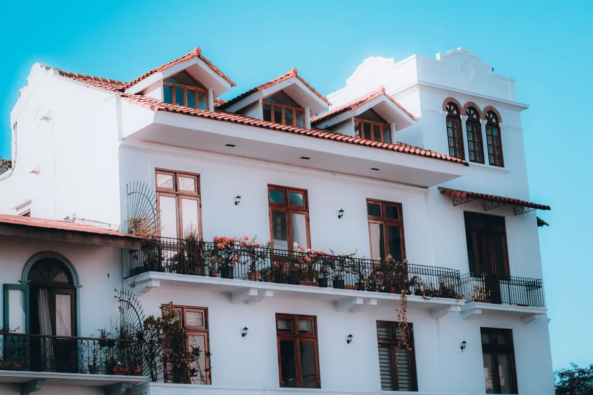 Fachada blanca de un edificio con balcones de hierro, ventanas de madera y tejado de teja