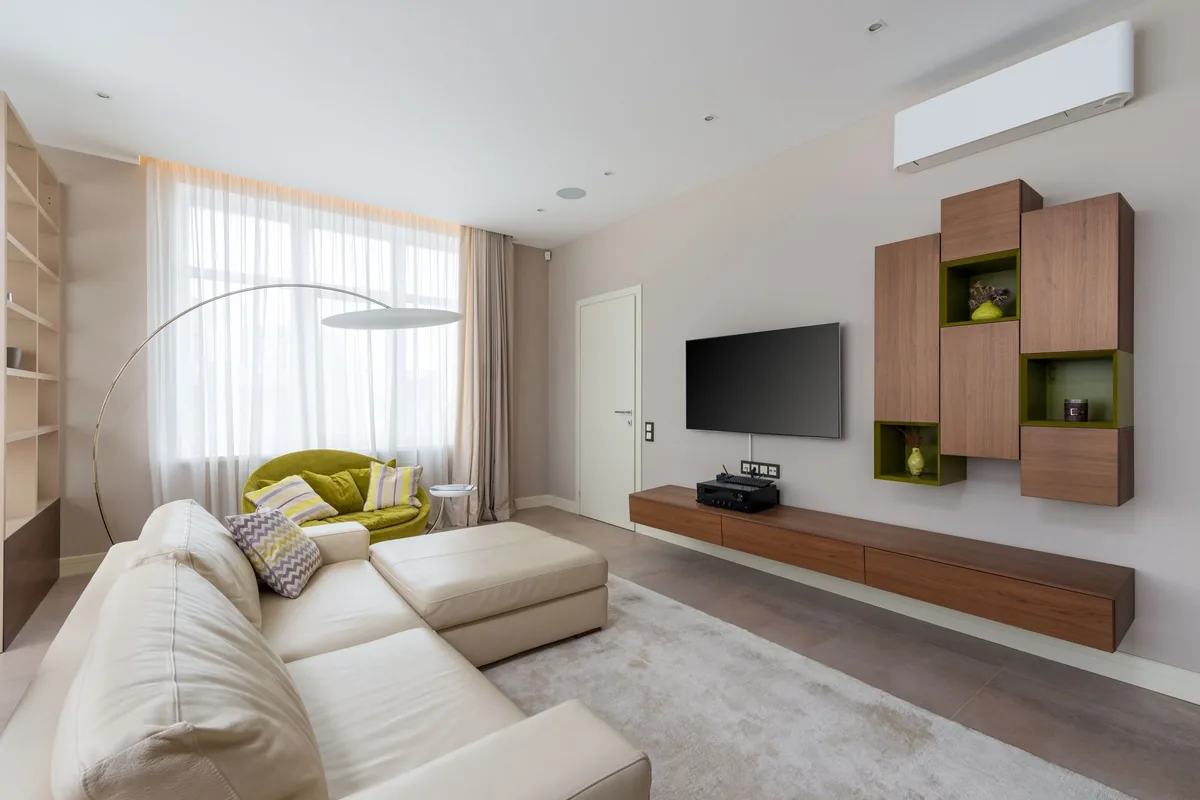 Salón con un sofá claro, una televisión en la pared y un split de pared blanco cerca del techo