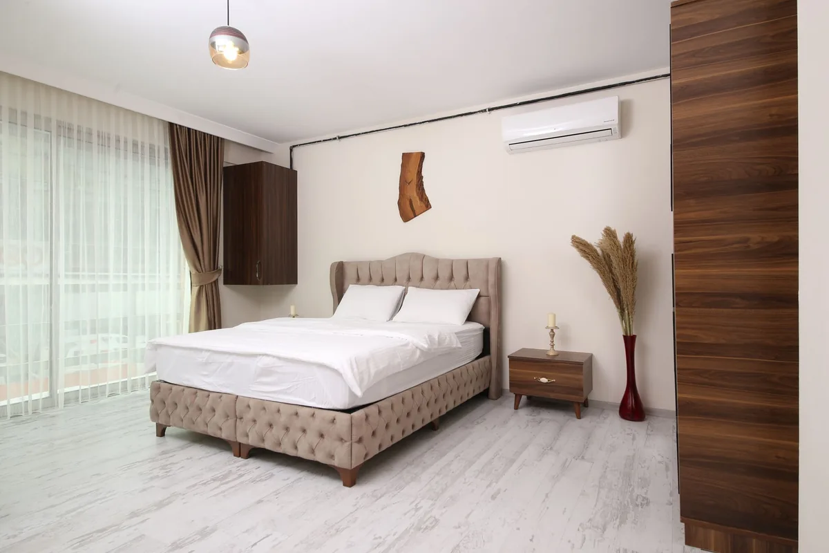Dormitorio con una cama doble y un aire acondicionado de pared en lo alto, junto a una ventana grande