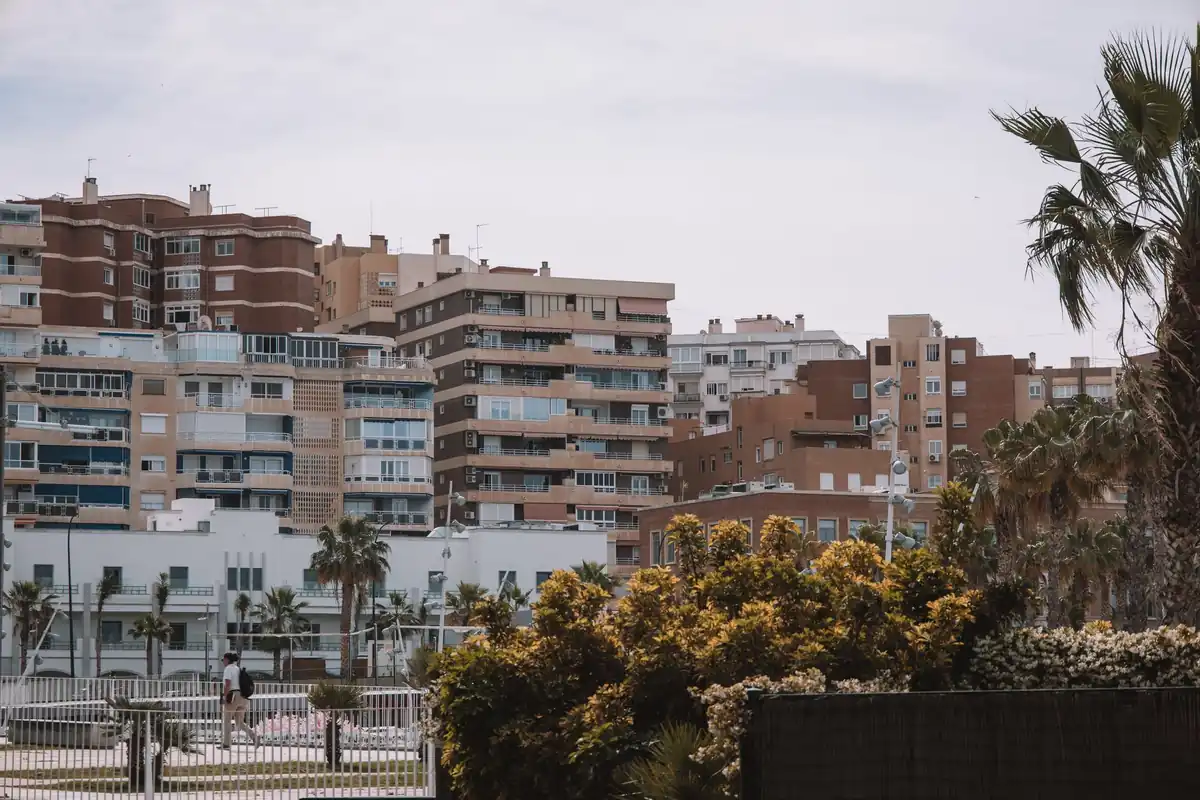 Bloques de apartamentos de ladrillo y color claro con balcones, palmeras y arbustos en una zona de costa