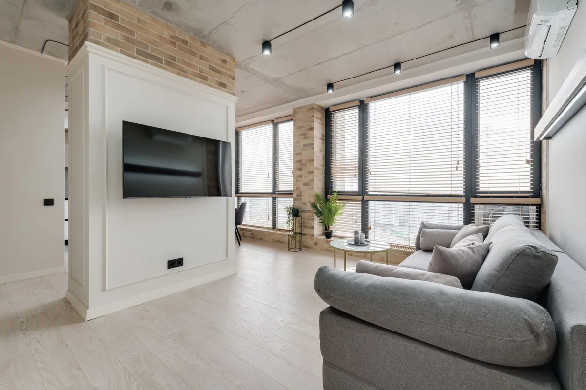 Salón con un sofá gris, una televisión en la pared y un split en lo alto a la derecha