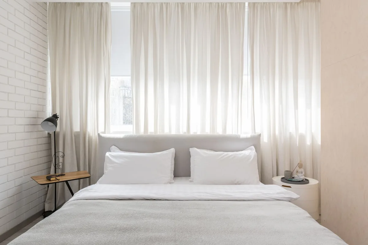 Dormitorio luminoso con cama de ropa blanca y cortinas de lino claras ante la ventana
