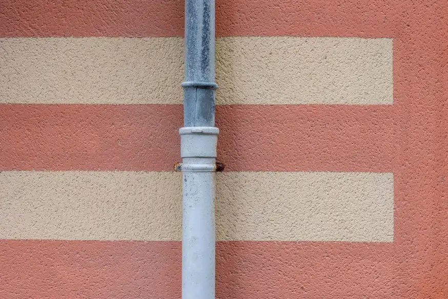 Tubo de bajante gris sobre una fachada de bandas rojizas y beige