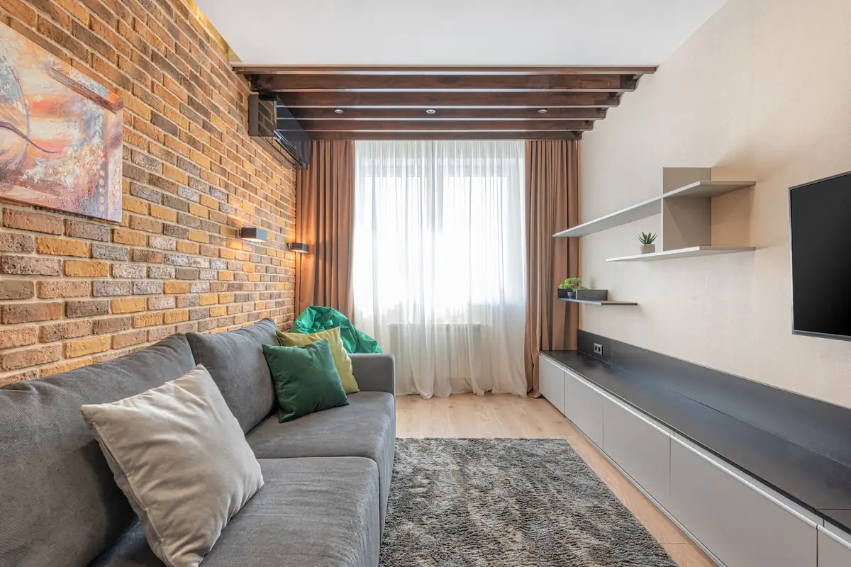 Salón con pared de ladrillo visto, vigas de madera en el techo y un split de pared oscuro en lo alto